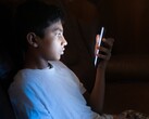Teenager in a dark room looking at a glowing smartphone