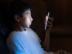 Teenager in a dark room looking at a glowing smartphone