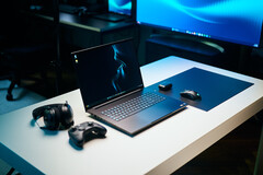Razer Blade 18 2026 gaming laptop setup on a white desk with glowing RGB keyboard, mouse, gaming controller, and headphones in a dark studio setting.