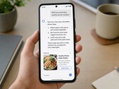 A hand holding a smartphone showing an AI answer with a sponsored ad below it
