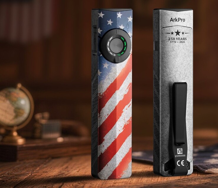 The Olight ArkPro Stars & Stripes Edition flashlight has a thumb switch with a three-way selector dial on the front and a metal pocket clip on the back.