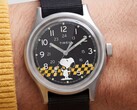 Close-up of the Timex MK1’s black dial showing Snoopy against a yellow-and-black checkered graphic with Arabic hour markers and luminous hands.