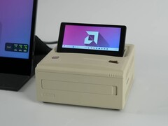 A retro-style Ayaneo AM01S mini PC in a beige finish, featuring a built-in flip-up secondary display showing the Windows desktop. (ETA Prime via YouTube)