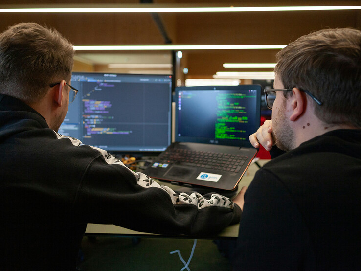 Researchers analyzing code on dual monitors (Image source: Flipsnack / Unsplash)