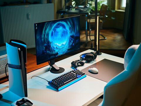 A clean studio gaming setup featuring the Sony Inzone M10S II monitor on a white desk alongside a vertical PlayStation 5 Pro console, mechanical keyboard, wireless mouse, and headset with subtle blue lighting.