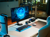 A clean studio gaming setup featuring the Sony Inzone M10S II monitor on a white desk alongside a vertical PlayStation 5 Pro console, mechanical keyboard, wireless mouse, and headset with subtle blue lighting.