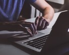 Hands typing on a MacBook keyboard in low light, the Apple logo glowing