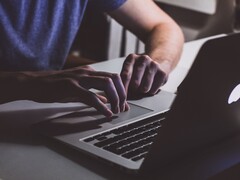Hands typing on a MacBook keyboard in low light, the Apple logo glowing