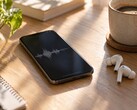 Smartphone displaying an audio waveform beside wireless earbuds and a coffee cup on a wooden desk