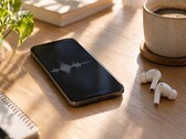 Smartphone displaying an audio waveform beside wireless earbuds and a coffee cup on a wooden desk