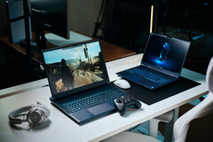 Two gaming laptops sitting on a white desk displaying detailed path-traced game footage next to a controller, mouse, and headset in a studio room.