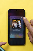 A OnePlus smartphone displaying the media player widget, with a user tapping the audio output icon to access Bluetooth audio-sharing controls.