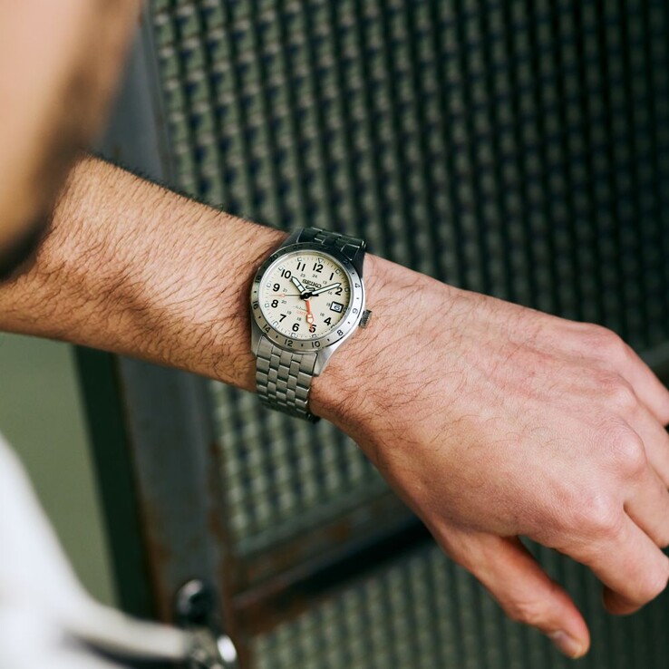 Front view of the Seiko 5 Sports Field GMT HDB002 with a cream dial, orange GMT hand, fixed 24-hour bezel, and stainless steel bracelet.