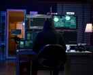 A hooded researcher works across multiple screens in a darkened setup. Generic hacker pictured.