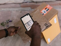A hand holds a smartphone over a parcel and scans its barcode