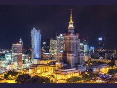 Nighttime cityscape of Warsaw featuring the illuminated Palace of Culture and Science surrounded by modern skyscrapers and office buildings. (Source: Kamil Gliwiński via Unsplash)