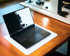 An open matte black Razer Blade 16 gaming laptop sitting on a white desk mat over a warm wooden table, displaying a vivid black-and-white wallpaper.