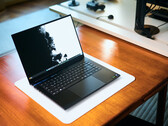 An open matte black Razer Blade 16 gaming laptop sitting on a white desk mat over a warm wooden table, displaying a vivid black-and-white wallpaper.