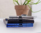 Stack of foldable smartphones representing the concept of the upcoming Apple iPhone Fold, placed on a white table with a potted plant in the background (Image source: Notebookcheck)