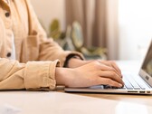 Hands typing on the keyboard of an open laptop at a bright desk
