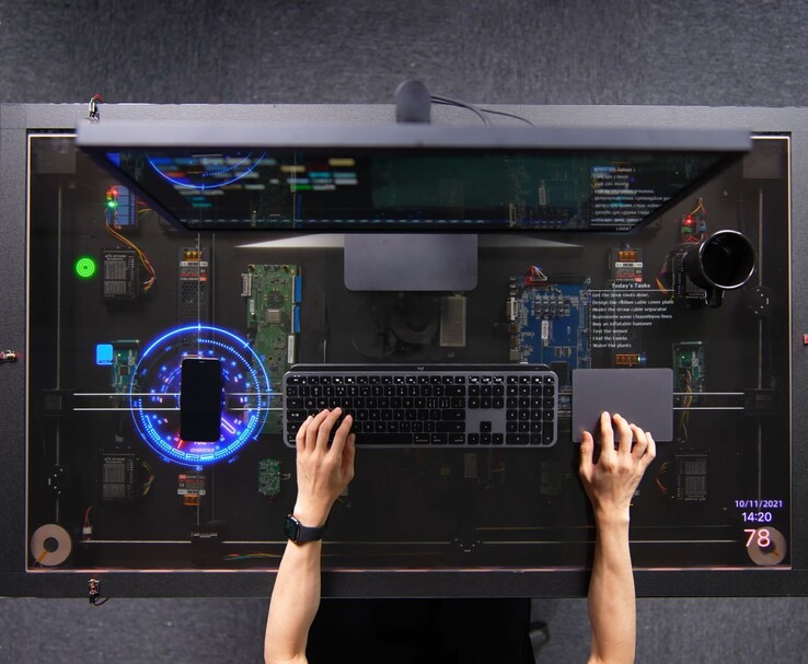 HTX Studio’s DIY AirPower-inspired desk in use, with a phone charging on the transparent display alongside a keyboard, trackpad and monitor.