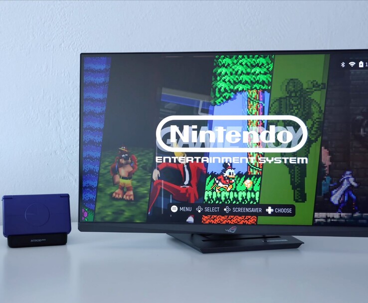 Retroid Pocket Flip 2 in purple placed on a dock next to a monitor, with the TV screen showing a retro NES emulator interface. (Image source: Retro Game Corps on YouTube)