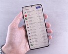 A hand holds a smartphone that shows a list of updates on screen.