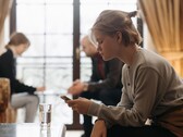 A teenager looks at her smartphone, with two adults sitting out of focus in the background.