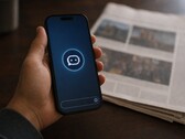 A hand holds a smartphone showing a chatbot icon, a printed newspaper lies next to it.