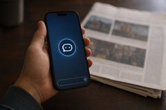 A hand holds a smartphone showing a chatbot icon, a printed newspaper lies next to it.