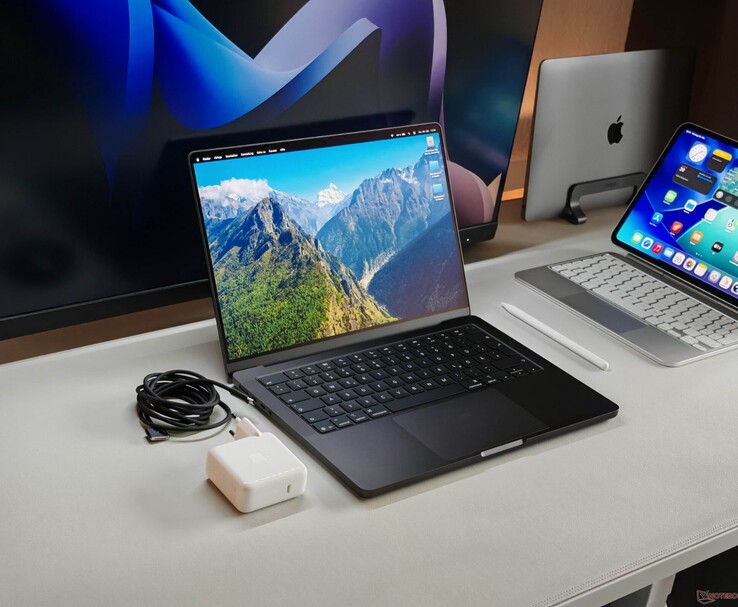 Apple MacBook Pro shown on a desk with charger and external displays (Image source: Notebookcheck)
