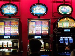 Slot machines inside a casino with bright illuminated displays and people playing in front (Image source: djedj via Pixabay)
