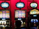 Slot machines inside a casino with bright illuminated displays and people playing in front (Image source: djedj via Pixabay)