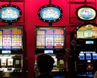 Slot machines inside a casino with bright illuminated displays and people playing in front (Image source: djedj via Pixabay)