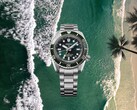 Seiko Prospex HBC001 diver’s watch with green dial and bezel displayed over an aerial beach and ocean background.