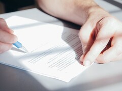 A hand signs a document with a blue ballpoint pen