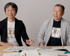 A screengrab of Shigru Miyamoto and Tezuka Takashi wearing Super Mario Bros. 30th anniversary t-shirts