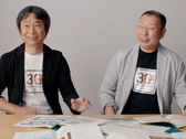 A screengrab of Shigru Miyamoto and Tezuka Takashi wearing Super Mario Bros. 30th anniversary t-shirts