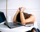 Woman looking down at her smartphone with a laptop beside her