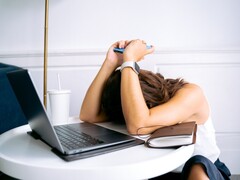Woman looking down at her smartphone with a laptop beside her