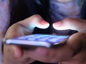 Two hands hold a smartphone with a glowing screen in the dim light