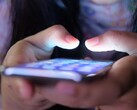 Two hands hold a smartphone with a glowing screen in the dim light