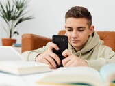 Teenager in a hoodie typing on a smartphone with open school books in front of him