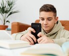 Teenager in a hoodie typing on a smartphone with open school books in front of him