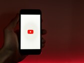 A hand holding a smartphone with the YouTube logo lit up on the display against a red background