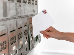 A hand putting an envelope into a row of letterboxes
