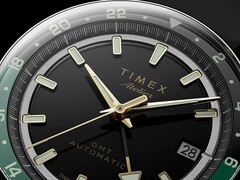 Close-up of the Timex Atelier GMT Première M1a’s black dial with gold-tone hands, luminous hour markers, date window, and black-and-green 24-hour GMT ring.