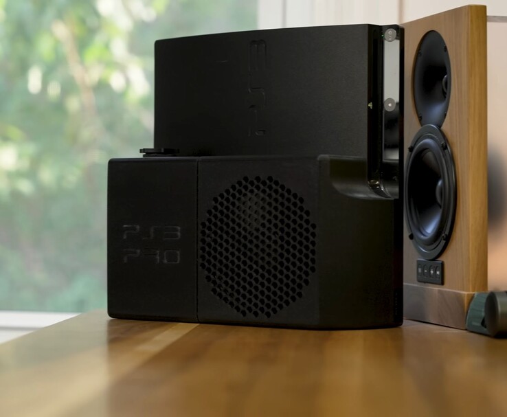 Water-cooled PlayStation 3 with a black 3D-printed “PS3 Pro” rear housing beside a wooden speaker. (Image source: Zac Builds via YouTube)