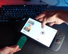 Yu from YouTube channel Better Gaming holding a Nintendo Switch 2 in one hand and an open-source green PCB adapter in the other, attempting to insert it into the device's microSD Express slot (Image source: Better Gaming via YouTube)