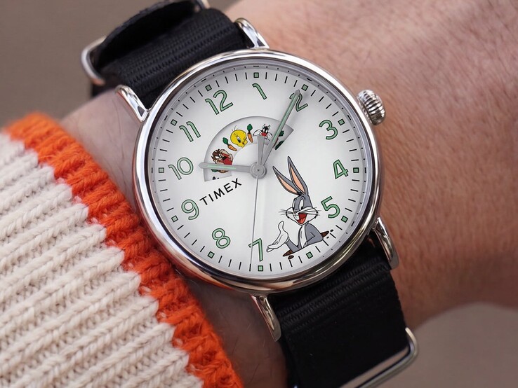 Timex Looney Tunes watch displayed on a wrist, showing its white dial, rotating character window, green-accented numerals, and black fabric strap.
